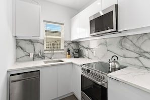 A modern kitchen with white cabinetry, a built-in oven, a microwave, and a kettle. - Hyde Park 1/1 private residence 3 (Tampa)
