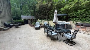 Un patio con mesa y sillas, una parrilla y un muro de piedra.