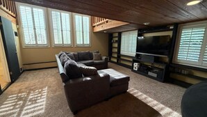 Una sala de estar con un sofá modular, un televisor de pantalla plana y una estantería.