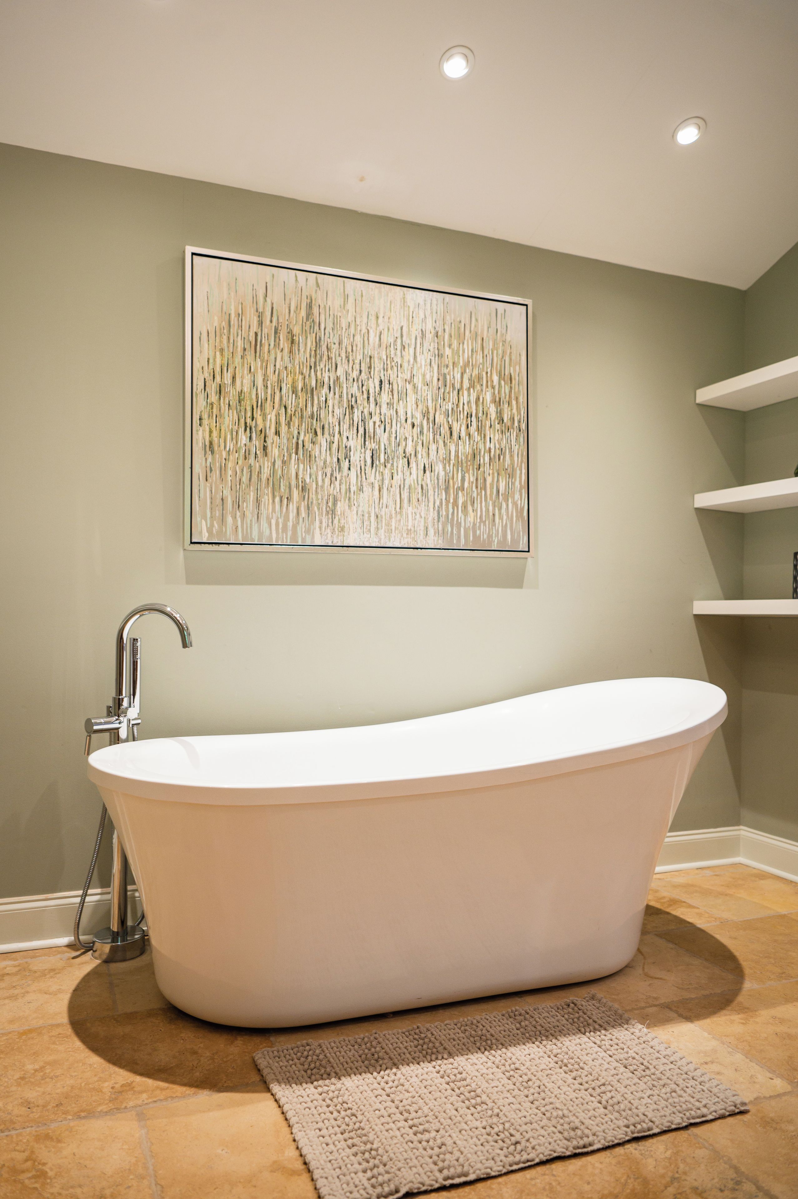 A freestanding bathtub in a bathroom with a textured wall art piece above it.