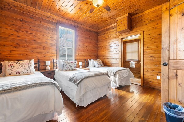 Una cabaña con dos camas, paredes de madera, un ventilador de techo y un ventanal.