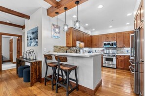 A modern kitchen with wooden cabinets, a central island, bar stools, and stainless steel appliances. - Ski In/Out Beaver Creek I Slopeside Retreat W/Pool (Avon)
