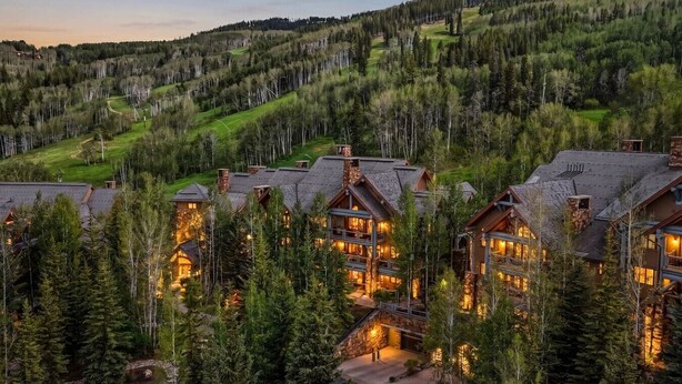 Un chalet comprenant plusieurs bâtiments, entouré d’arbres et situé dans un paysage vallonné.