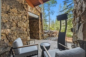 Ein Außenbereich mit Steinsitzen, einem Kamin aus Stein und Blick auf den umliegenden Wald.