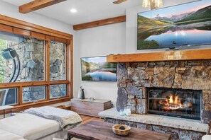 A cozy living room with a stone fireplace, large windows, and a flat-screen TV. - Ski In/Out Beaver Creek I Slopeside Retreat W/Pool (Avon)