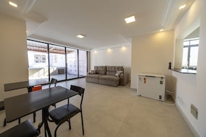 Ein Zimmer mit Esstisch, Stühlen, einer Couch, einem Kühlschrank und einem großen Fenster.