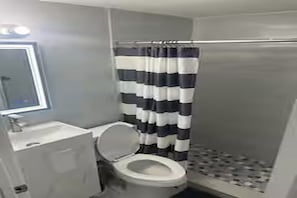 A bathroom with a toilet, a sink, and a shower with a striped curtain. - Cozy 2-bedroom house in perfect Port Richey with AC (Port Richey)