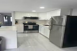 A modern kitchen with white cabinets, stainless steel appliances, and a black refrigerator. - Cozy 2-bedroom house in perfect Port Richey with AC (Port Richey)