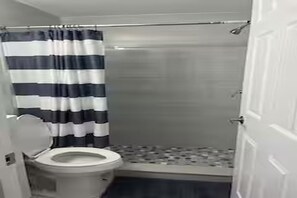 A bathroom with a toilet, a shower stall, and a striped shower curtain. - Cozy 2-bedroom in perfect Port Richey with AC (Port Richey)