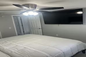 A bedroom with a bed, a ceiling fan, a TV mounted on the wall, and a door. - Cozy 2-bedroom house in perfect Port Richey with AC (Port Richey)