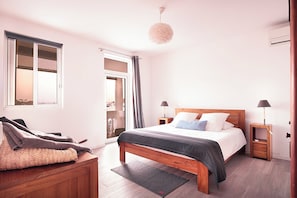 Une chambre à coucher avec un lit, des tables de chevet, un banc en bois, une fenêtre et une porte.