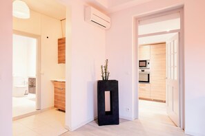 Un couloir avec un pot de fleurs noir, un meuble en bois et un appareil de climatisation.