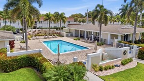 A pool area with lounge chairs, palm trees, and a building with a sign reading 'BLUE SOUTH.' - Beach Proximity Condo w/ Pool & Dining Access (Naples)