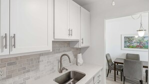 A modern kitchen with white cabinets, a brick backsplash, and a stainless steel sink. - Beach Proximity Condo w/ Pool & Dining Access (Naples)