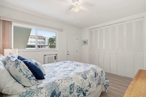 Ein Schlafzimmer mit Bett, Deckenventilator, Fenster, Tür und Kleiderschrank.