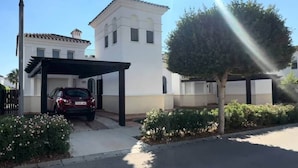Un edificio residencial con cochera cubierta, un árbol y cielo despejado.