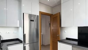 Una cocina moderna con electrodomésticos de acero inoxidable, armarios blancos y una puerta de madera que da a otra habitación.