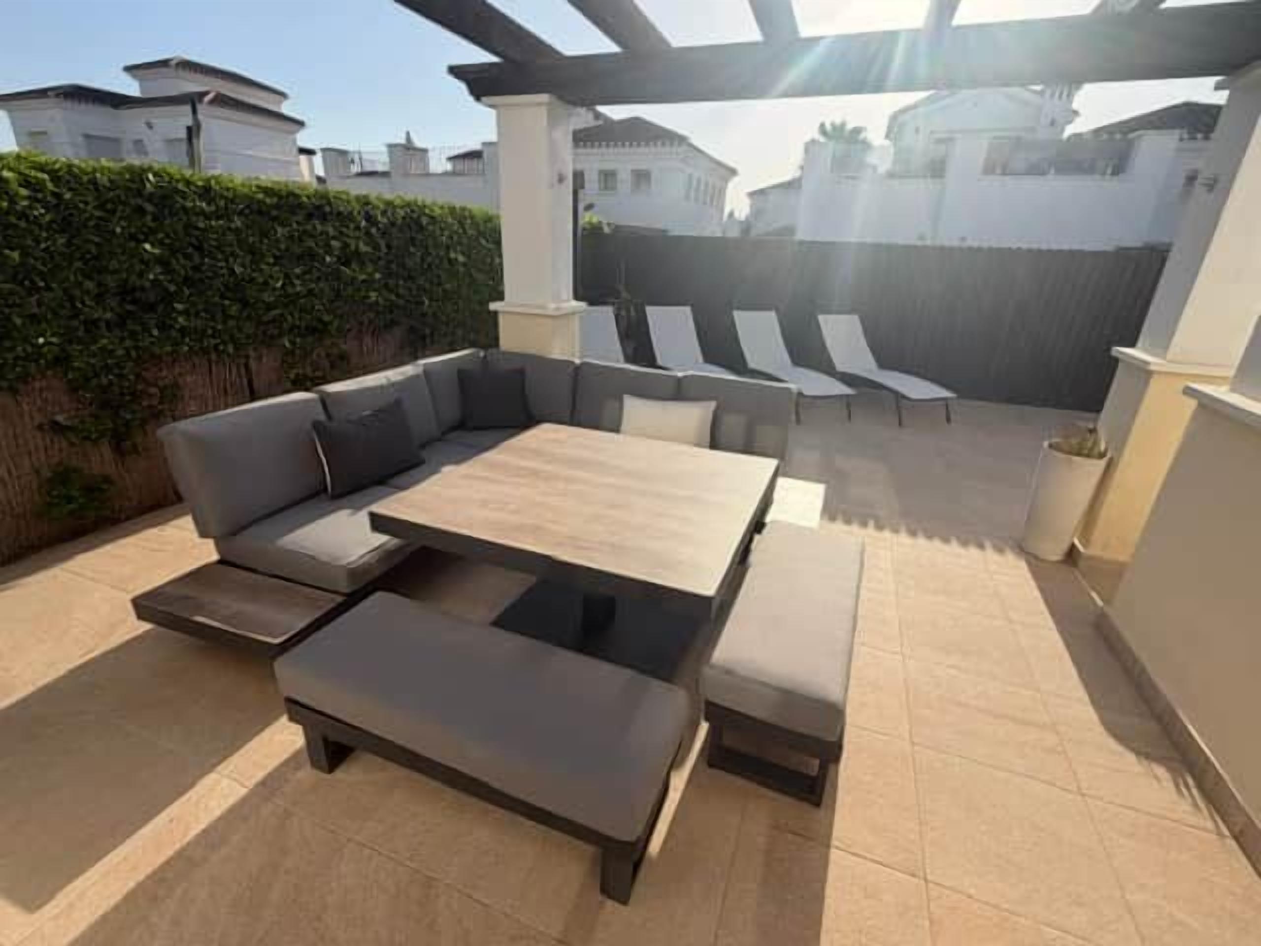 Un patio al aire libre con un sofá modular, una mesa de centro y sillones.