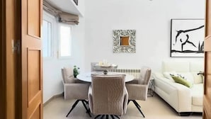 Una sala de estar moderna con comedor, un sofá blanco, un espejo decorativo y un cuadro en la pared.