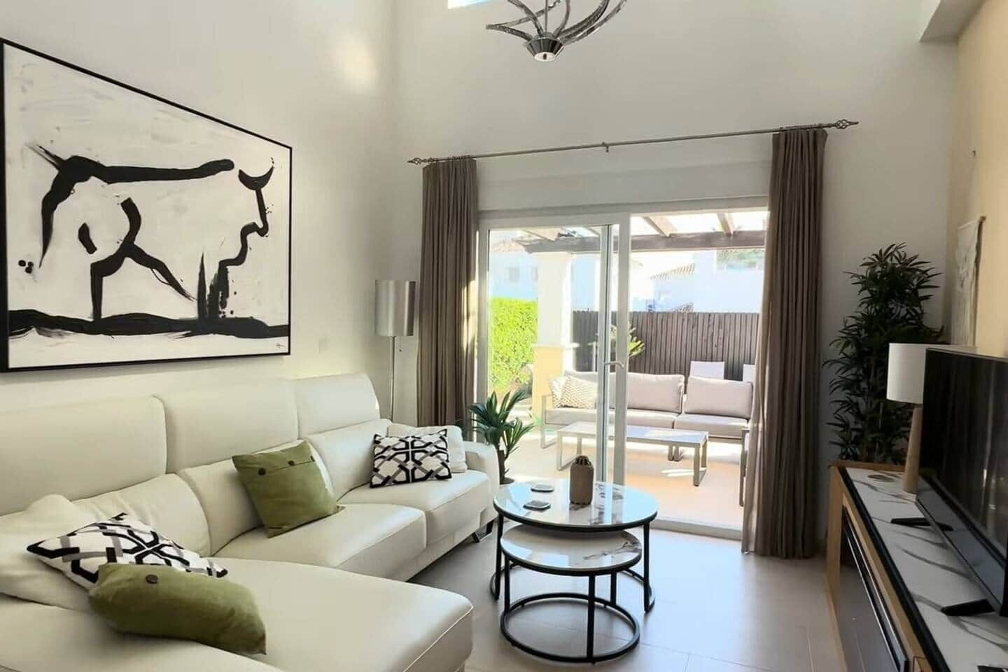 Una sala de estar con un sofá, una mesa de centro, un televisor y un gran ventanal corredizo que da a un patio exterior.