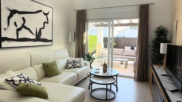 Una sala de estar con un sofá, una mesa de centro, un televisor y un gran ventanal corredizo que da a un patio exterior.