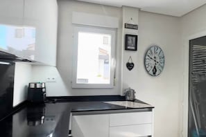 Eine kleine Küche mit schwarzem Arbeitsplatz, weißen Schränken, einem Fenster und einer Wanduhr.