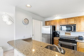A kitchen with granite countertops, stainless steel appliances, wooden cabinets, and a clock on the wall. - 1 Bedroom Beachfront Condo! (Old Orchard Beach)