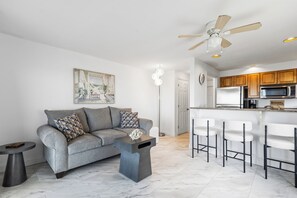A modern living room with a grey sofa, a coffee table, and a ceiling fan. - 1 Bedroom Beachfront Condo! (Old Orchard Beach)