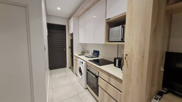 A compact kitchen with a washing machine, a microwave, and a built-in oven. - Explore Zimbali Whilst Staying at Zimbali Lakes (Ballito)