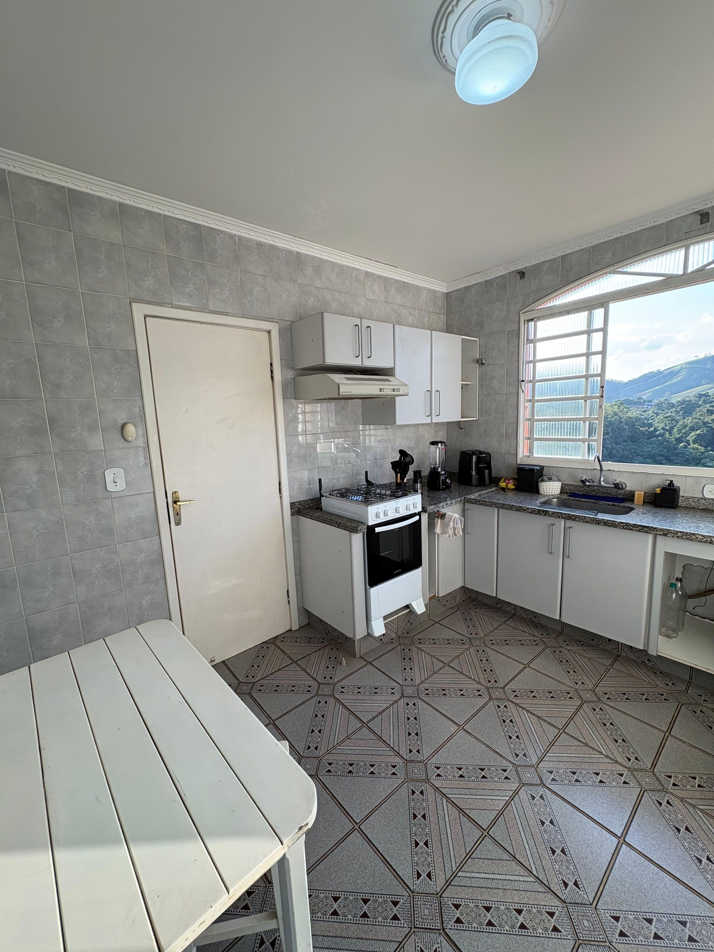 Eine Küche mit Gasherd, Backofen, weißen Schränken, einem Fenster mit Aussicht und einem Musterfliesenboden.