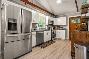 Una cocina con electrodomésticos de acero inoxidable, armarios blancos y una viga de techo de madera.