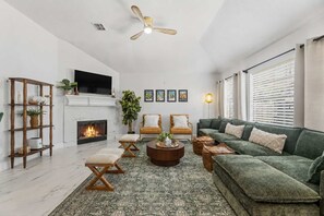 Ein modernes Wohnzimmer mit Kamin, einem grünen Sofa, einem Holztisch und einem an der Wand befestigten Fernseher.