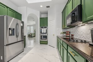 A modern kitchen with green cabinets, stainless steel appliances, and a herringbone tile backsplash. - 4 Themed Rooms | 11 Min to Universal Kids (Frisco)