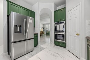 A kitchen with green cabinets, a stainless steel refrigerator, and a white door. - 4 Themed Rooms | 11 Min to Universal Kids (Frisco)