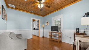 A living room with a sofa, a TV on a stand, a ceiling fan, and a kitchen in the background. - Hill Country Retreat Near Gruene & Rivers (New Braunfels)