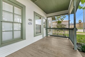 A white building with a green door and windows, a porch with a metal railing, and a number '435' on the wall.