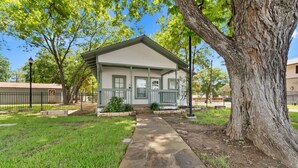 A single-story house with a front porch, a stone pathway leading to the entrance, and a large tree to the right. - Hill Country Retreat Near Gruene & Rivers (New Braunfels)