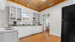 A kitchen with white cabinets, a black refrigerator, and a wooden ceiling. - Hill Country Retreat Near Gruene & Rivers (New Braunfels)