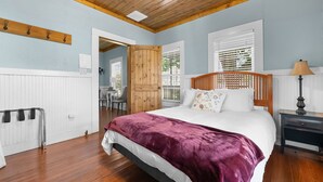 A bedroom with a wooden ceiling, a bed with a purple blanket, a nightstand, and a window with blinds. - Hill Country Retreat Near Gruene & Rivers (New Braunfels)
