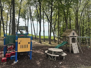 Ein Spielplatz mit Rutsche, Klettergerüsten und einem Picknicktisch in einem bewaldeten Gebiet.