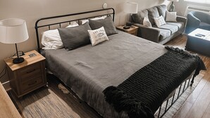 A bedroom with a bed, bedside tables, a lamp, a chair, and a small table. - Cozy Resort Condo in Bellaire- Golf, Ski, Lake & Family Fun (Bellaire)