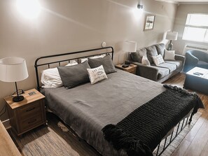 Ein Schlafzimmer mit Bett, Nachttischen, einer Lampe, einem Sessel und einem kleinen Tisch.
