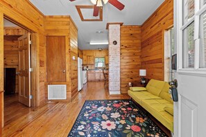 Ein Holzhaus-Interieur mit Holzboden, einem gelben Sofa, einem floralen Teppich und einer Küchenzeile.