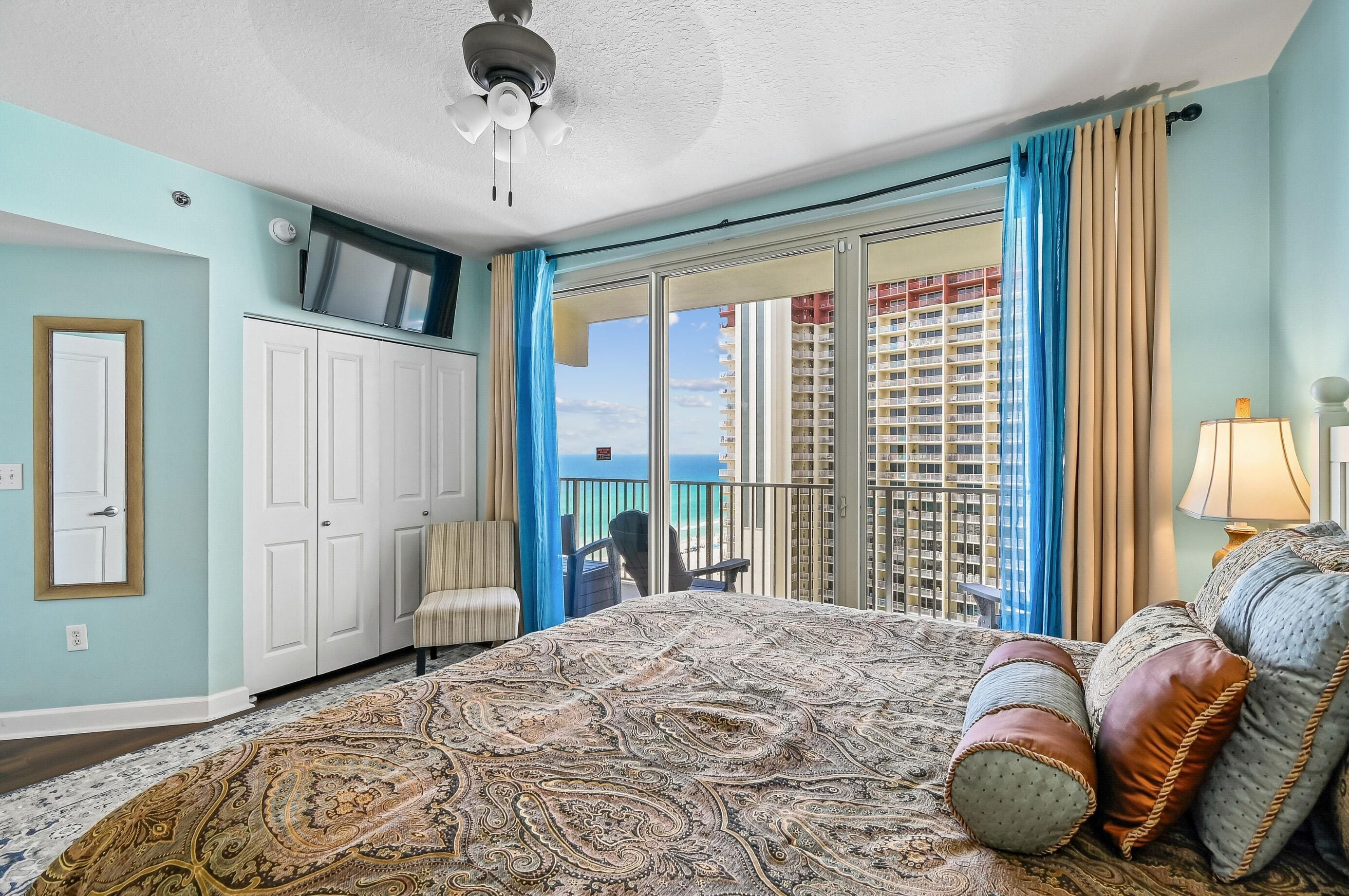 Ein Hotelzimmer mit einem großen Bett, einem Fernseher auf einer Kommode, einem Balkon mit Blick auf die Stadt und einem Sessel am Fenster.
