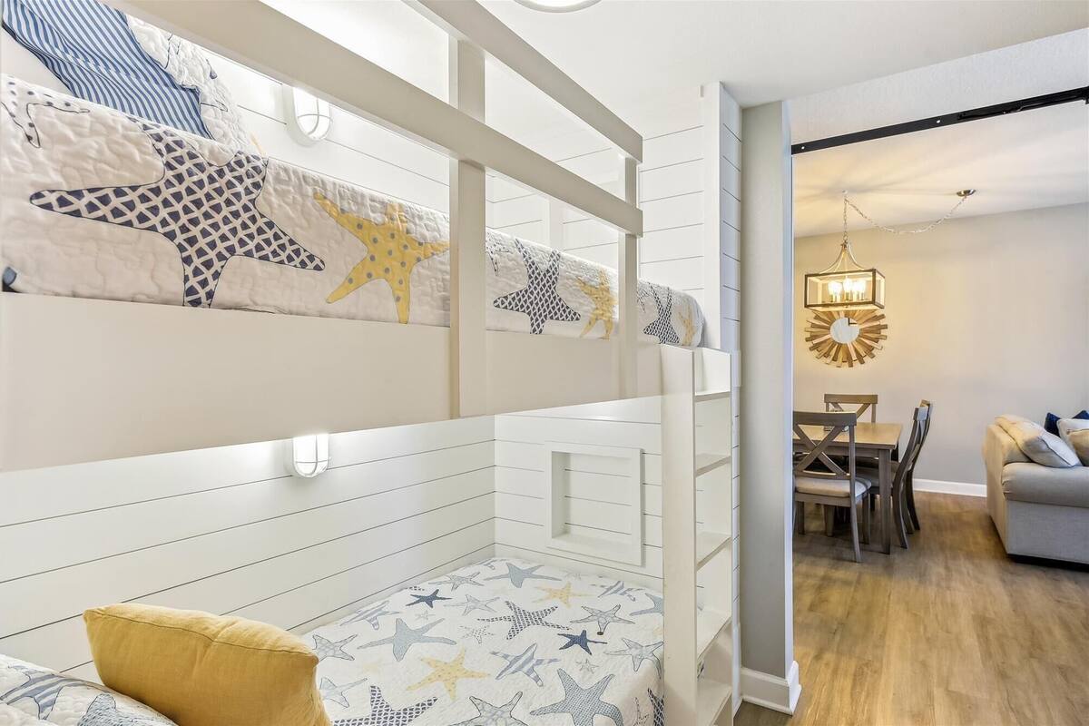 Ein Etagenbett mit Sterndruck, ein Essbereich mit einer Chandelüster und ein Sofa in einem modernen Interieur.