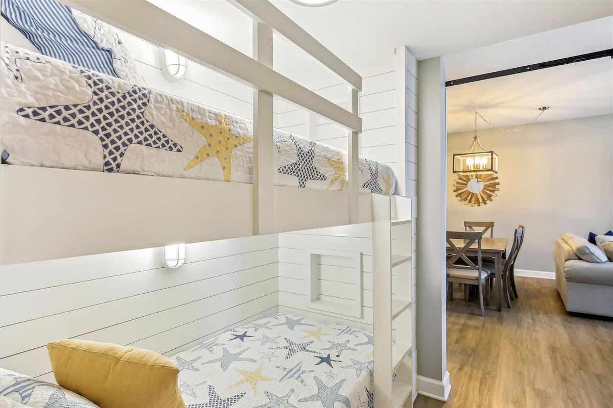 A bunk bed with star-patterned bedding, a dining area with a chandelier, and a sofa in a modern interior.