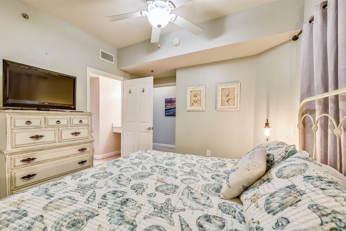 Ein Schlafzimmer mit Bett, Kommode, Deckenventilator und Bildern an der Wand.