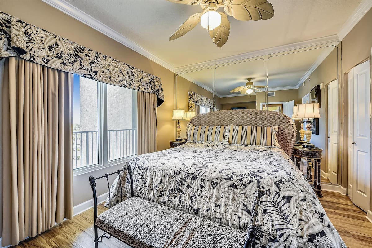 A spacious bedroom with a large bed, a chaise lounge, and a ceiling fan.