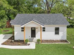 A single-story house with a front porch, a black door, and a small front yard with plants.