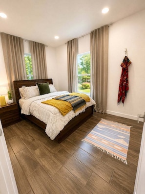 A bedroom with a wooden bed, a bedside table, a rug, and a window with curtains.